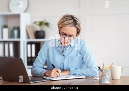 Beschäftigte junge Frau, die sich während eines Geschäftstreffens oder Online-Webinars Notizen macht und von zu Hause aus an einer Konferenz teilnimmt Stockfoto