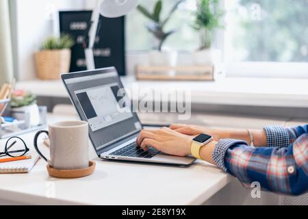 Cropped Frau tippen auf Laptop-Computer, während zu Hause sitzen. Nahaufnahme Kaffeetasse und menschliche Hände. Fernunterricht Online-Bildung und Arbeit Stockfoto