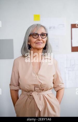 Vorderansicht der schönen älteren Frau Architektin, die drinnen zu Hause steht. Stockfoto