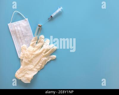 Impfstoff, Maske, Spritze, Handschuhe auf blauem Hintergrund - medizinische Ausrüstung zur Impfung gegen die Viren Stockfoto