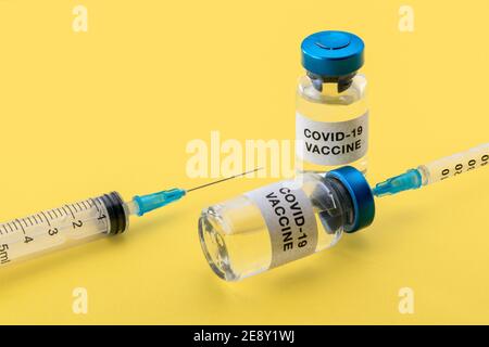 Coronavirus-COVID-19-Impfstoff. Fläschchen mit Spritzen isoliert auf gelbem Hintergrund, Konzeptkomposition mit Kopierraum Stockfoto