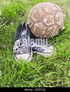 Alte Kinder Turnschuhe und ein zerrissener Ball - Hof Amateur Fußball Stockfoto