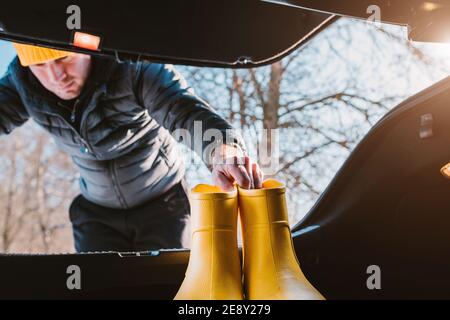 Ein Mann lädt gelbe Gummistiefel in den Kofferraum von Ein Auto für einen Spaziergang außerhalb der Stadt in der Woods - eine touristische Reise Stockfoto