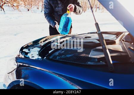 Ein Mann öffnete die Haube und gießt eine Frostschutzscheibe Flüssigkeit in den Tank - ein Scheibenwischer im Winter Stockfoto