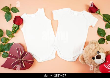 Happy Valentine's Day Baby Kleidung Flatlay owith Teddybär, rote Rosen und herzförmigen Geschenk auf modernen Korallen Hintergrund. Modell mit negativer Kopie sp Stockfoto