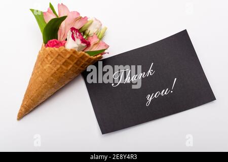 Draufsicht auf Blumen in Waffelkegel neben Karte mit Dankesschriftzug auf Weiß Stockfoto