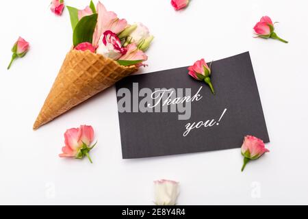 Draufsicht auf rosa Blumen in Waffelkegel neben Karte Mit Dankesschriftzug auf weiß Stockfoto