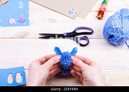 How to make a bunny from pom-poms for Easter decor. Children's art project. DIY concept. Hands make a blue Easter bunny out of a pompom. Step by step Stockfoto
