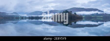 Rydal fiel und die Küste von Grasmere spiegeln sich in den spiegelruhigen Gewässern des Sees an einem bewölkten Morgen mit Nebel, der zwischen den Fjells driftet. Stockfoto