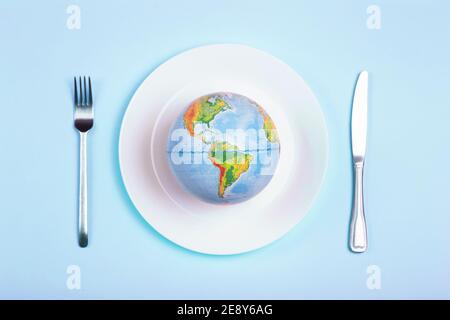 Globus auf einem Teller für Lebensmittel auf blauem Hintergrund. Macht, Wirtschaft, Politik, Globalismus, Hunger, Armut und Welternnahrungskonzept. Stockfoto