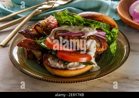 Griechischer gefüllter truthahn-Burger mit Gurkenscheiben und Tsatziki gekrönt Joghurtsauce serviert mit mediterranen Street Cart frittierten Kartoffeln mit Feta-Chees Stockfoto