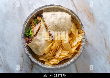 Takeout Dose gegrilltes Hähnchenwickel mit Frühlingsmischung Balsamico Dressing Und Kartoffelchips auf der Seite Stockfoto
