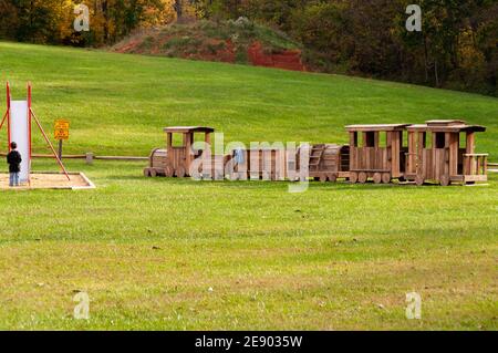 Der 4-6-jährige kaukasische Junge steht vor einer Slipper-Rutsche in einem Spielpark mit einem großen Holzzug. USA. Stockfoto