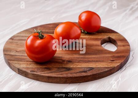 Drei rote Tomaten auf einem runden Küchenbrett aus Akazienholz, eine hinter der anderen Stockfoto