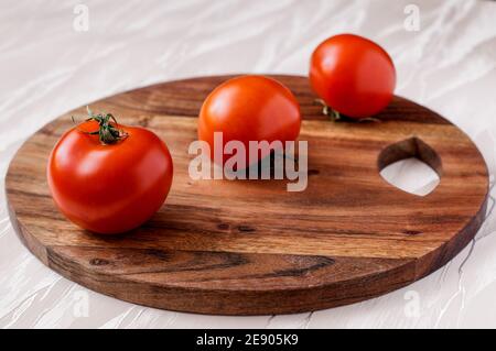 Drei rote Tomaten auf einem runden Küchenbrett aus Akazienholz, eine hinter der anderen Stockfoto