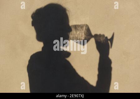 Schatten an der Wand einer Sommelierin allein mit einem Glas Wein. Mit einem gass of Wine Konzept Stockfoto