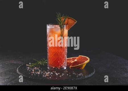 Pink Grapefruit Mezcal Paloma Cocktail aus Longdrinkglas mit Wassertropfen. Nahaufnahme, geringe Schärfentiefe, dunkler Hintergrund. Stockfoto