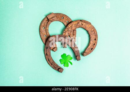 Schlecht abgenutzte Hufeisen mit Filzkleeblatt. Good Luck Symbol, St.Patrick's Day Konzept. Matt türkisfarbener Hintergrund, Draufsicht Stockfoto