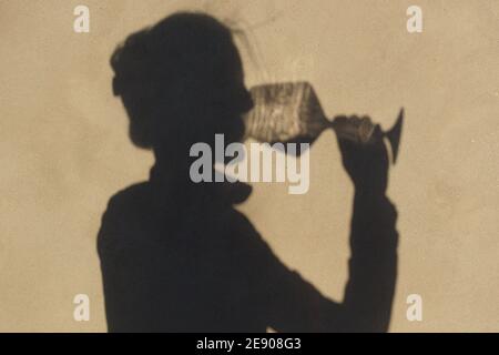 Schatten an der Wand einer Sommelierin allein mit einem Glas Wein. Mit einem gass of Wine Konzept Stockfoto