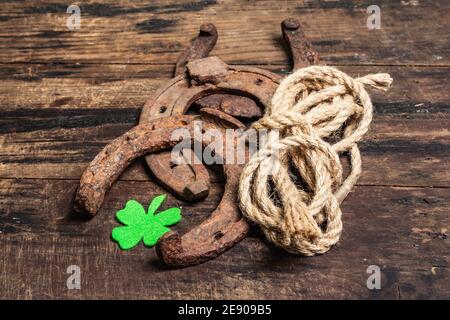 Schlecht abgenutzte Hufeisen, Seil und Filzkleeblatt. Good Luck Symbol, St.Patrick's Day Konzept. Vintage Holzbretter Hintergrund Stockfoto