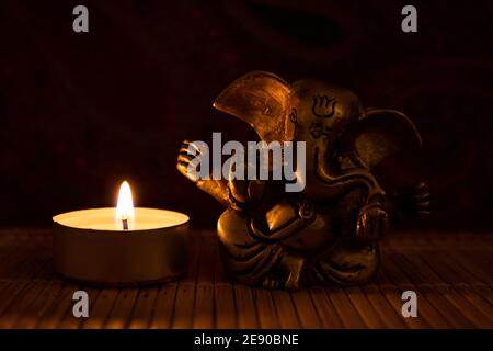 Ganesha-Statue mit angezündeter Teelichtkerze auf Holzoberfläche Stockfoto