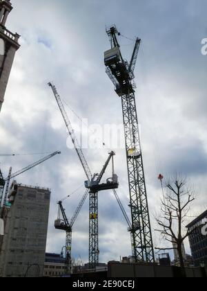 Hohe Turmdrehkrane auf einer Baustelle in London verkrampften sich an einem trüben, bewölkten Wintertag im Februar gegen einen bewölkten Himmel Stockfoto