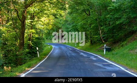 Leere kurvige Asphaltstraße im grünen Wald von Werbach, Deutschland. Malerische Aussicht auf leere Straße an einem sonnigen Tag. Stockfoto