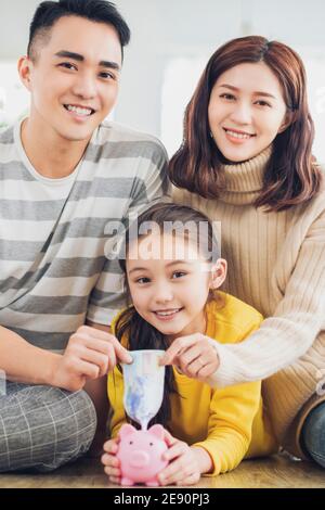 Vater, Mutter und Tochter halten Sparschwein und Geld zu Hause. Familie und sparen für zukünftige Konzept. Stockfoto