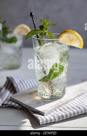 Erfrischendes Getränk mit Zitrone und Minze in einem Glas auf einem weißen Holzbrett, ein Getränk auf der Rückseite Stockfoto