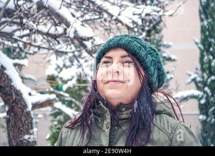 Frau mit Strickmütze im Freien im Garten beim Schneefall Stockfoto