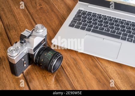 Eine alte 35 mm Spiegelreflexkamera auf einem Holztisch neben einem modernen Laptop, ein Kontrast zwischen modern und alt, horinzontal Stockfoto