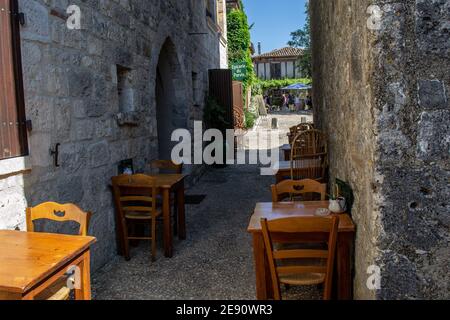 PUJOLS, FRANKREICH - 14. JULI 2019 : Restauranttische im Freien warten auf Leute, die nach dem Markt in einem schönen mittelalterlichen Dorf kommen Stockfoto