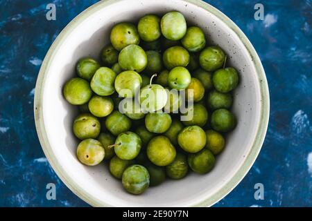 Gesunde pflanzliche Rezeptur Konzept, frische grüne Pflaumen in Obstschale auf blauem Hintergrund Stockfoto