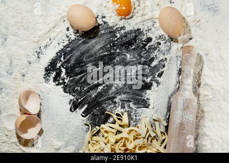 Frisch gekochte Pasta liegt auf einer dunklen, mit Mehl bestäubten Oberfläche. Italienische Pasta. Tagliatelle. Rohe Pasta. Italienische Pasta Rezept. Draufsicht, Kopierbereich Stockfoto