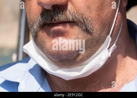 Schnurrbart Mann mit einer weißen schützenden medizinischen Maske, bis zum Kinn gesenkt. Falsches Tragen von medizinischen Masken unter Quarantäne. Nahaufnahme. Stockfoto