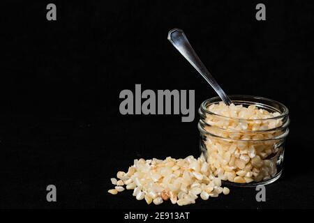 Zerbrochene weiße Maiskörner in einem Glasgefäß auf einer schwarzen Oberfläche. Stockfoto