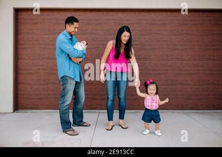 Asiatisch-amerikanische Mutter hilft Kleinkind Mädchen, während Papa hält watschelte Neugeborene Stockfoto