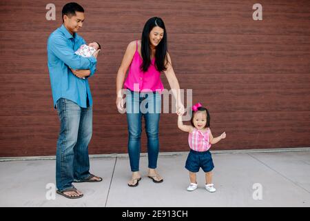 Glücklich asiatische Mutter hält Hand von Kleinkind, während Papa trägt Neugeborenes Stockfoto
