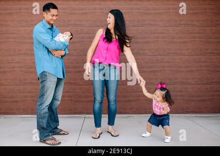 Kleinkind Mädchen tanzt für lachende Mama und Papa halten neue Baby Stockfoto
