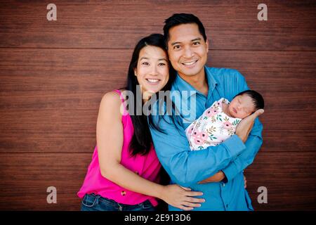 Glückliche asiatische Eltern mit neugeborenem Baby vor Holz Hintergrund Stockfoto