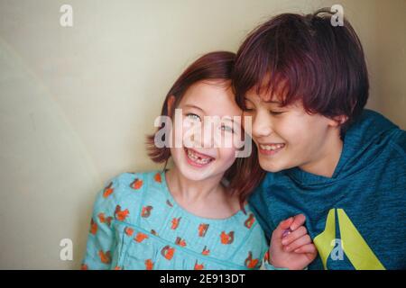 Zwei glückliche, lächelnde Kinder lehnen sich dicht an eine Wand Stockfoto