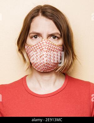 Ein Porträt einer Frau in einem roten Hemd und Maske schützt sie vor dem Coronavirus auf einem schlichten Hintergrund Stockfoto