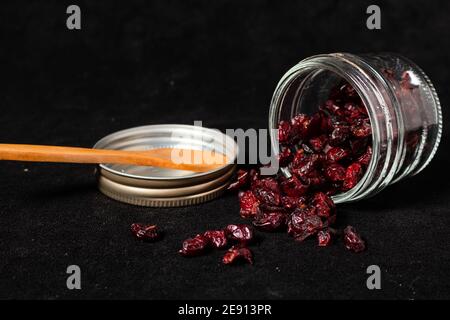 Getrocknete Preiselbeeren in einem Glas umgedreht auf einer schwarzen Oberfläche und der Deckel auf der Seite. Seitenansicht. Stockfoto