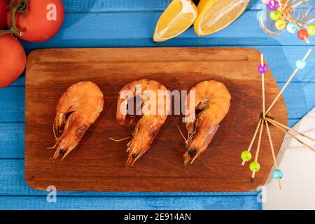 Ganze geröstete Garnelen auf einer Holzplatte auf einem blauen Tisch. Sommer Essen, frisch und natürlich. Stockfoto