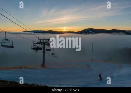 Sessellift für Skifahrer Bewegen auf dem Gipfel bei Sonnenuntergang Zeit und Foggy Day im Skigebiet Bukovel, Karpaten, Ukraine Stockfoto