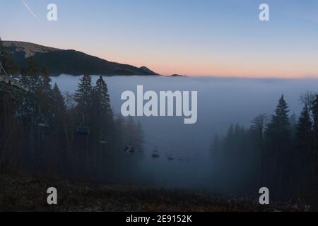 Sessellift für Skifahrer Bewegen auf dem Gipfel bei Sonnenuntergang Zeit und Foggy Day im Skigebiet Bukovel, Karpaten, Ukraine Stockfoto