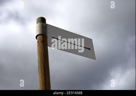 Detail eines weißen Schildes mit einem Pfeil in Form eines Wimpels, auf einem Holzmast mit einem bewölkten Himmel im Hintergrund. Stockfoto