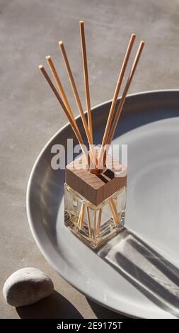 Handgefertigter Auffrischungsduft mit Bambusstäbchen-Diffusor und einer Flasche selbstgemachten Duftes. Zen-Steine, Aroma-Flasche auf einfache Keramik-Tablett aus weißem Stein Stockfoto