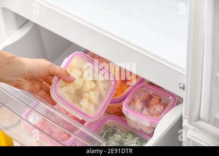 Frau, die Behälter mit gefrorenem Gemüse in den Kühlschrank stellt Stockfoto