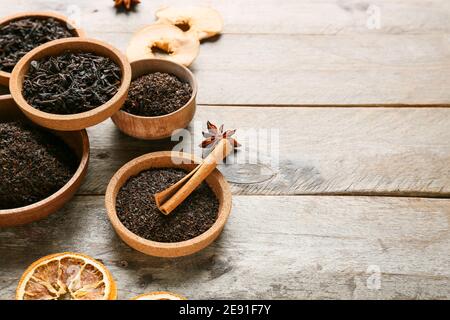 Schüsseln mit trockenen schwarzen Teeblättern, Gewürzen und getrockneten Früchten auf Holzgrund Stockfoto